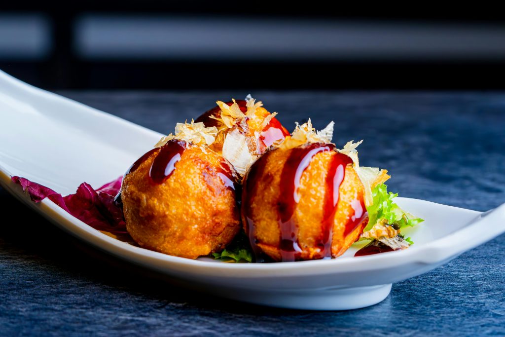 Crispy takoyaki balls drizzled with sauce on a white plate, a Japanese street food delight.