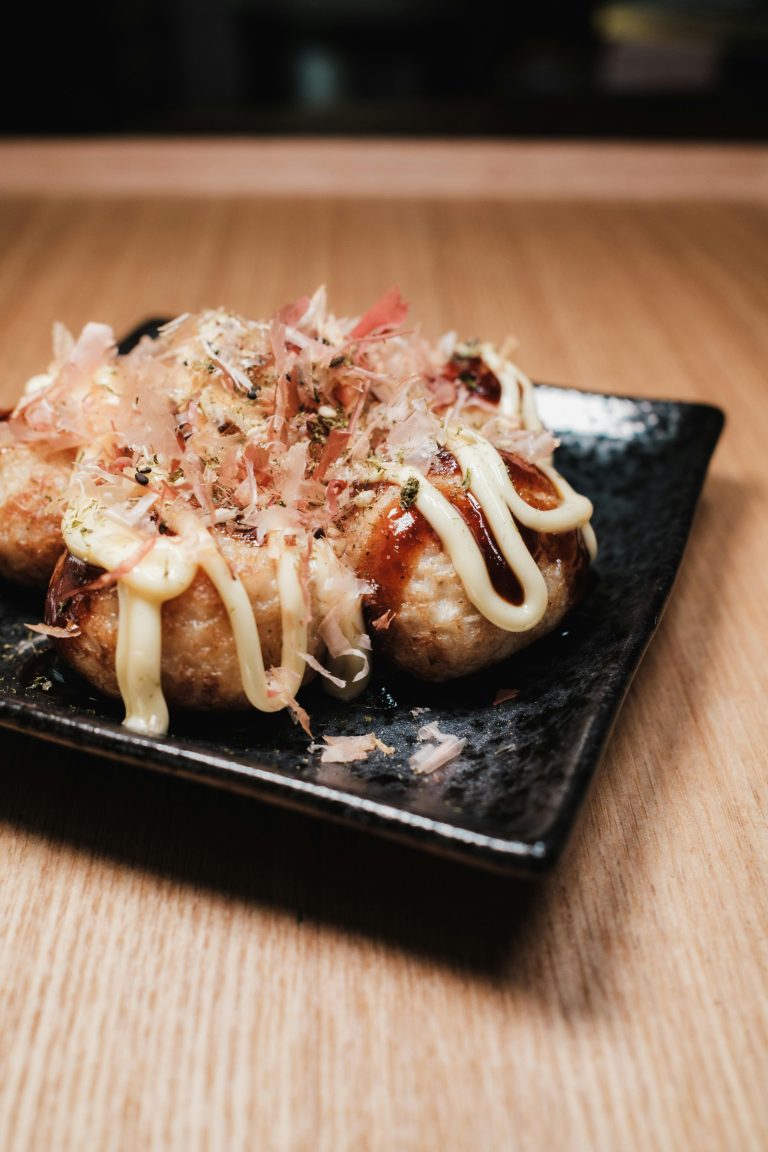 Appetizing takoyaki balls garnished with mayonnaise and bonito flakes on a black plate.